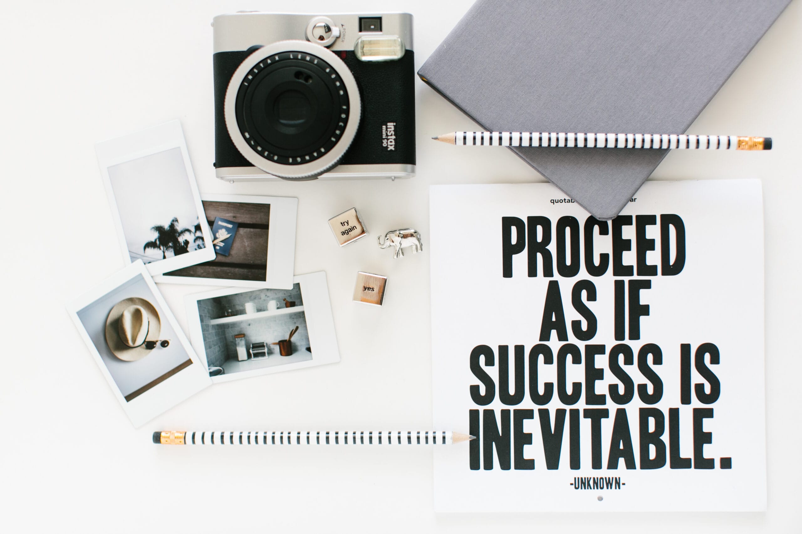 Flatlay of a camera and accessories with an uplifting quote saying "Proceed as if success is inevitable.